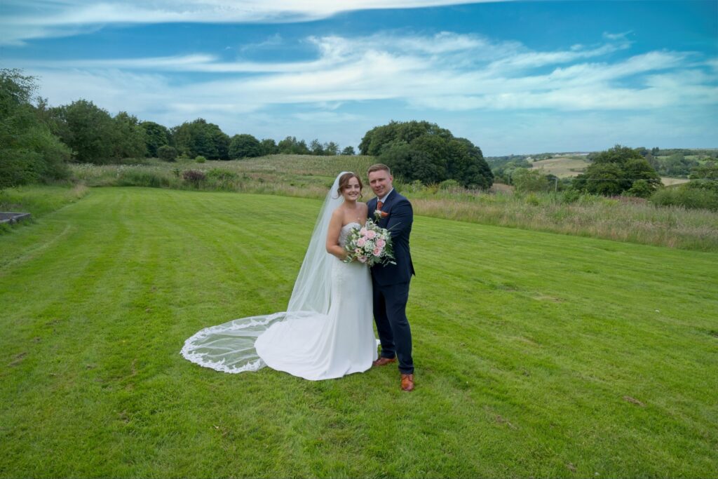 Bride and groom on a hillside lawn under a wide sky