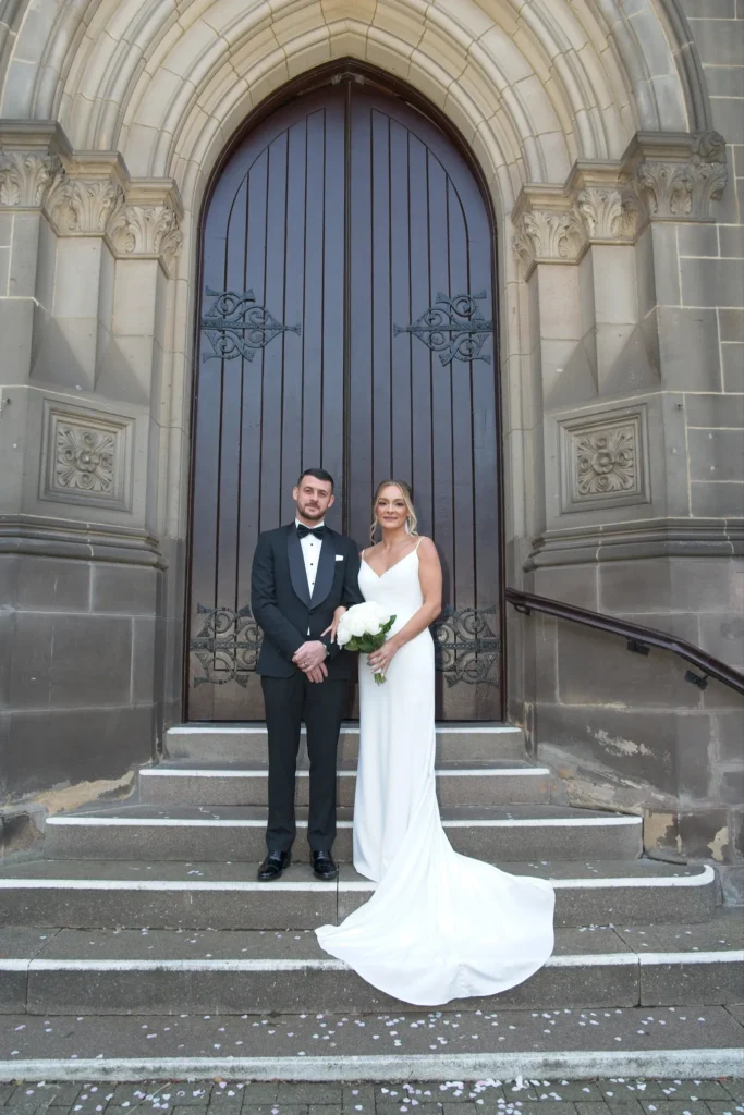 Bride and groom on stone steps in front of a tall arched wooden door