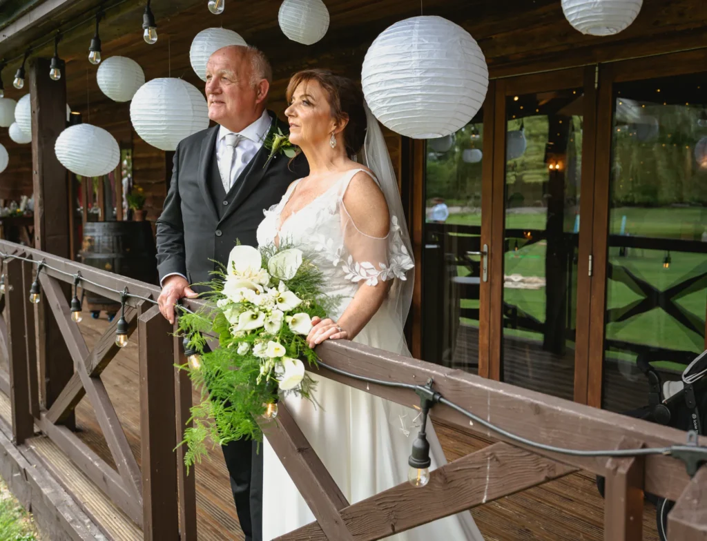 Bride and groom look out from a wooden balcony hung with white paper lanterns