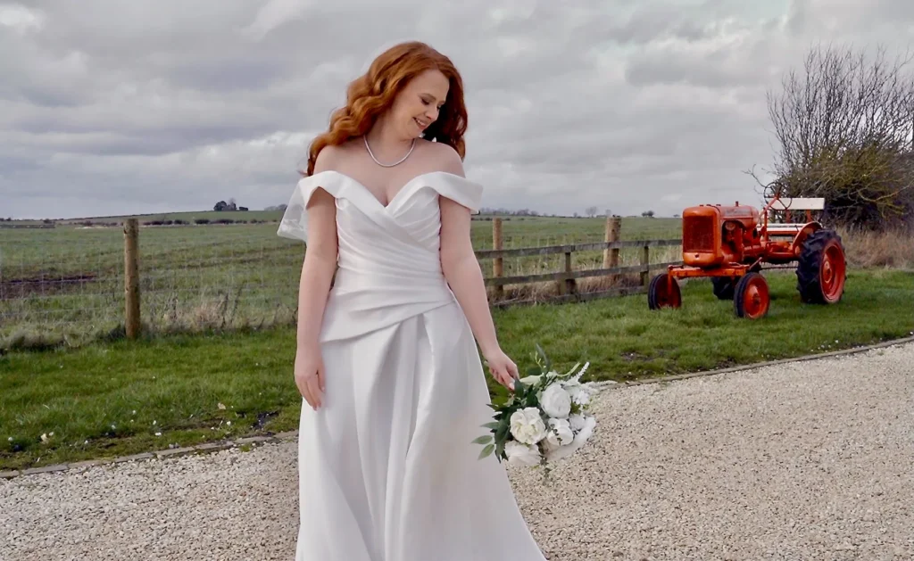 The bride with her bouquet on a farm drive, an orange vintage tractor behind