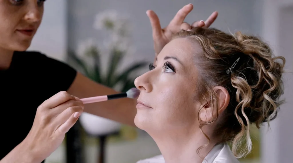 A make-up artist brushes powder onto the bride’s cheek as she gets ready