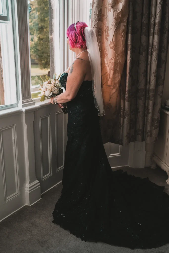 The bride in a dark green sequinned gown looks out of a tall window