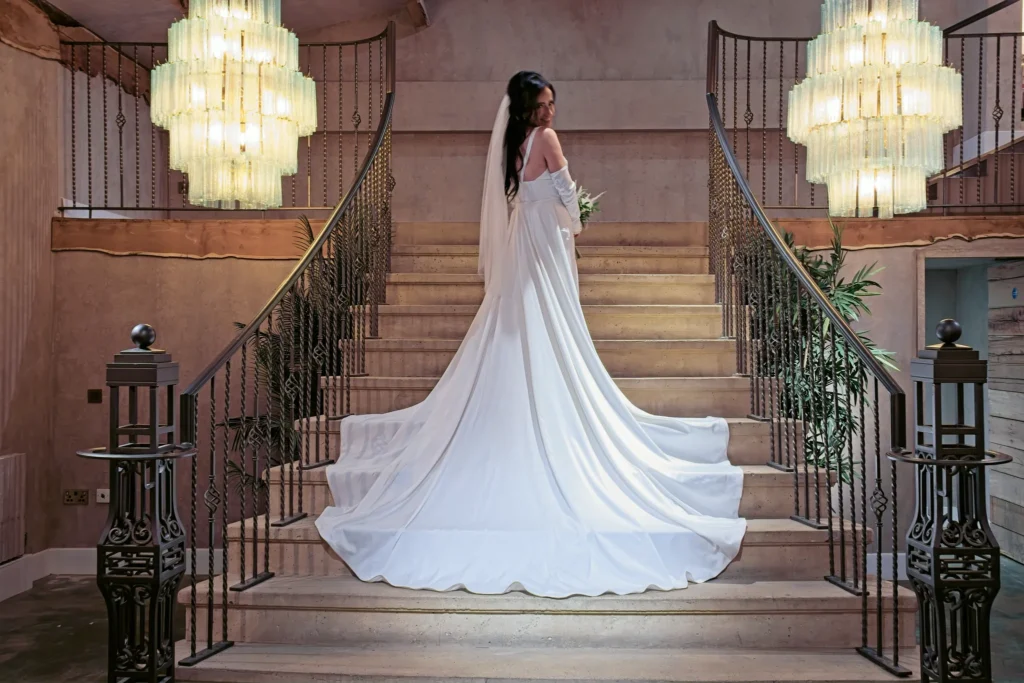 The bride looks back from a grand staircase, her long train across the steps