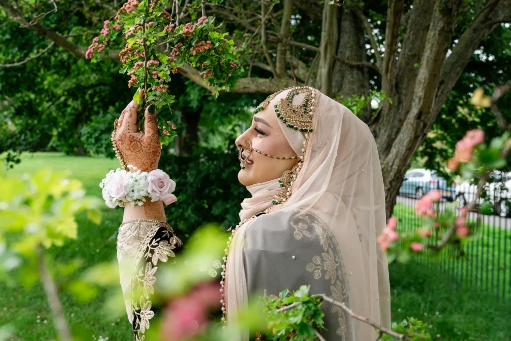 The bride at an Asian wedding, henna on her hands, reaches up to a branch of pink blossom