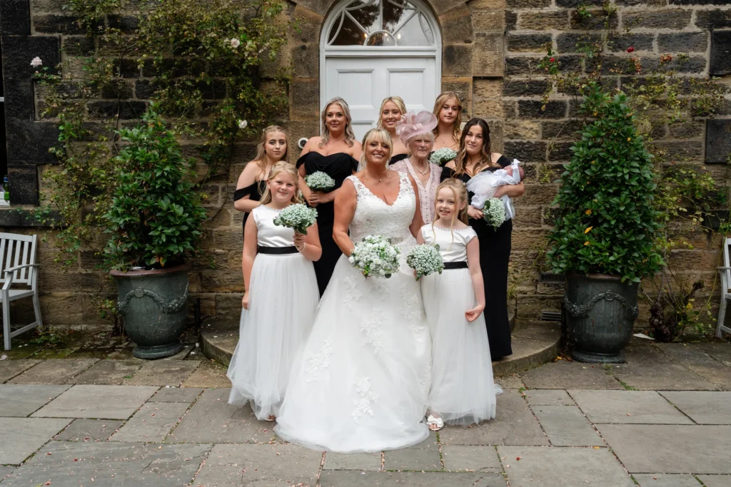 The bride with her bridesmaids, flower girls and family outside a stone house