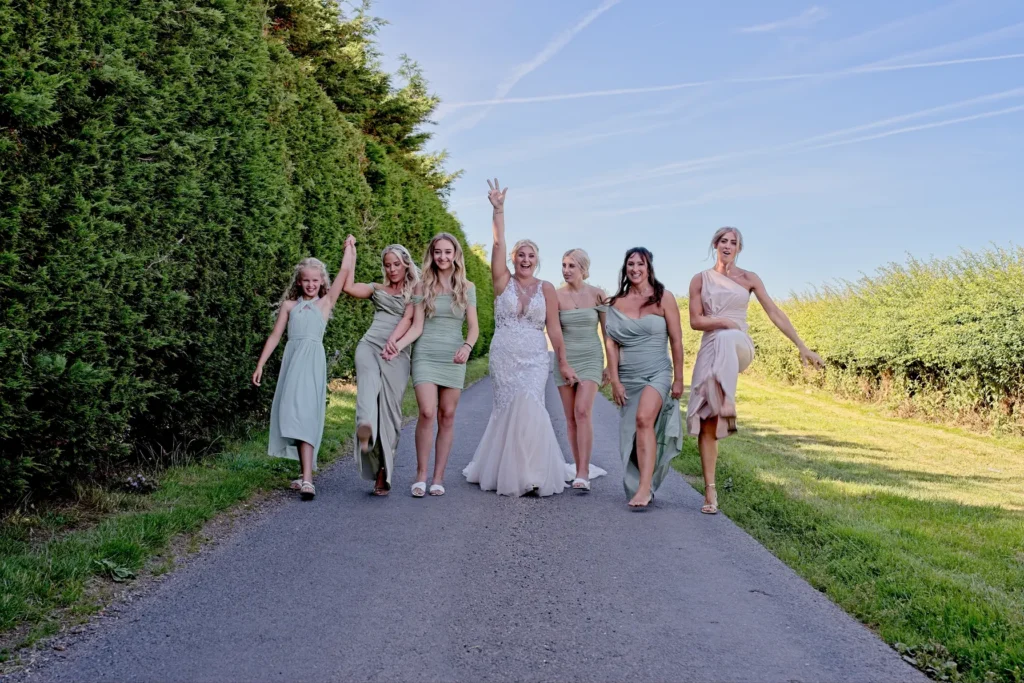 The bride and her bridesmaids dance down a country lane