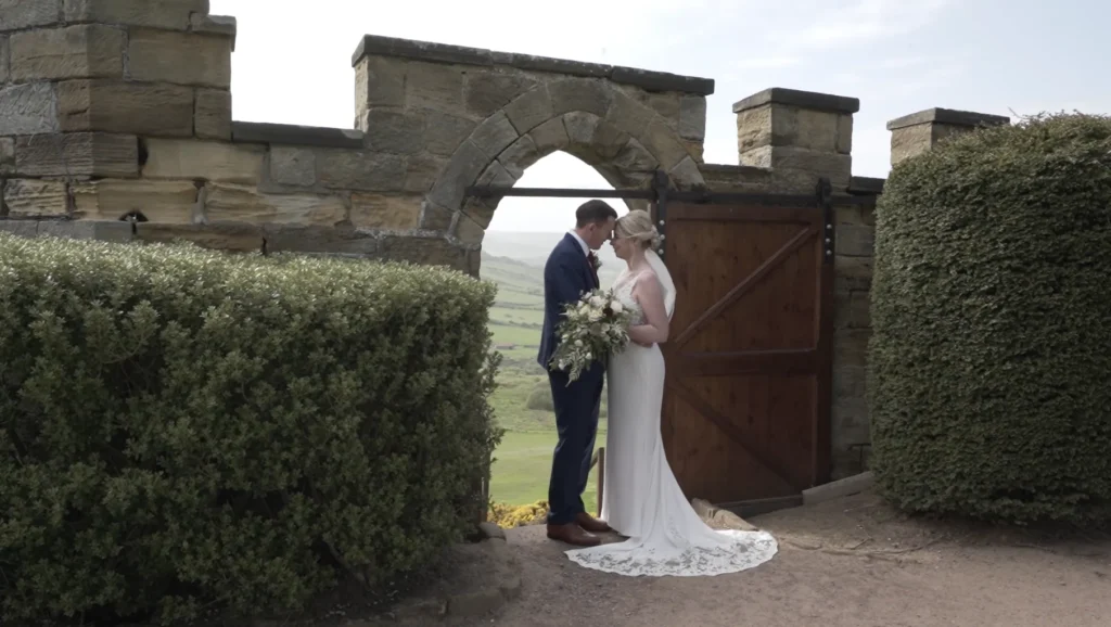 Bride and groom kiss in an arched gateway with the hills beyond
