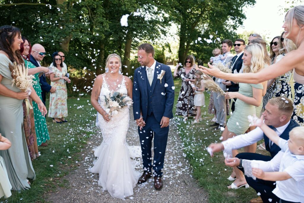 Bride and groom smiling as guests throw confetti
