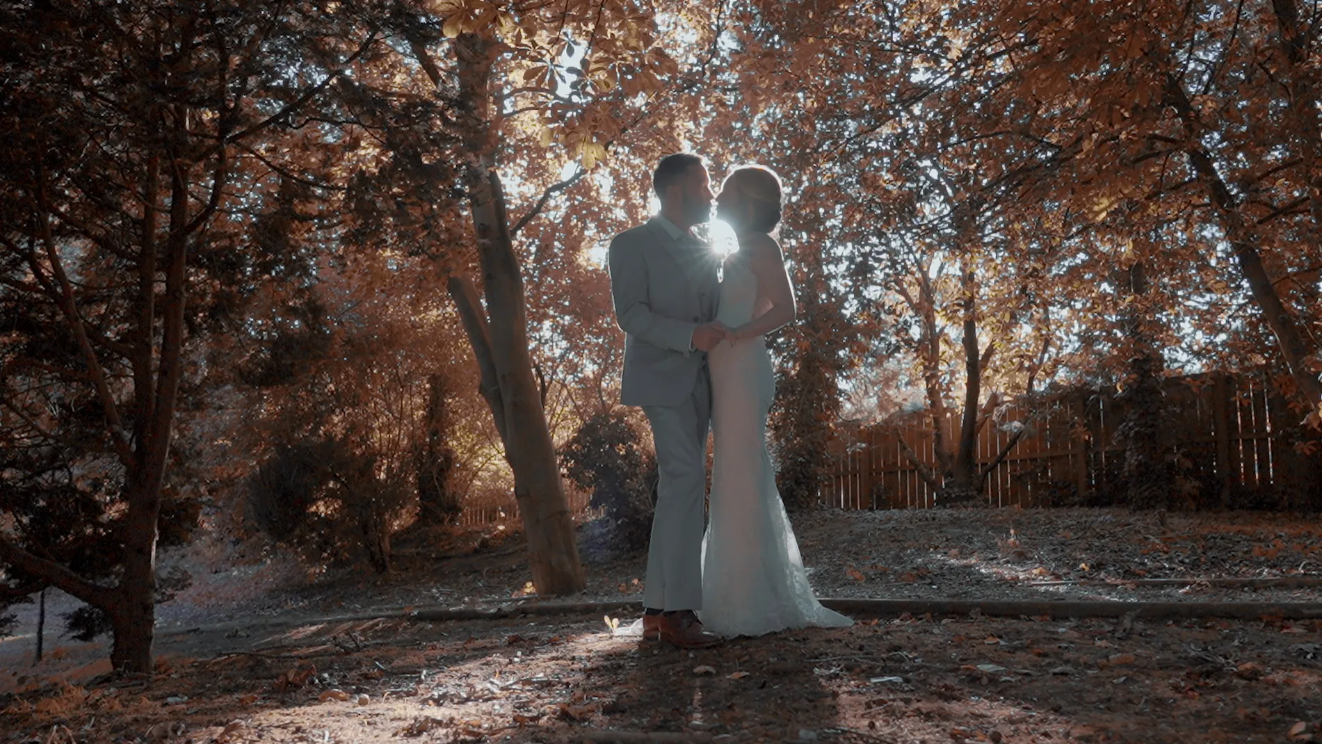 Bride and groom kiss among autumn trees, the low sun behind them