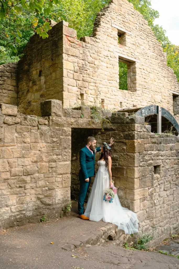 Bride and groom in the doorway of a ruined stone mill, its water wheel behind them