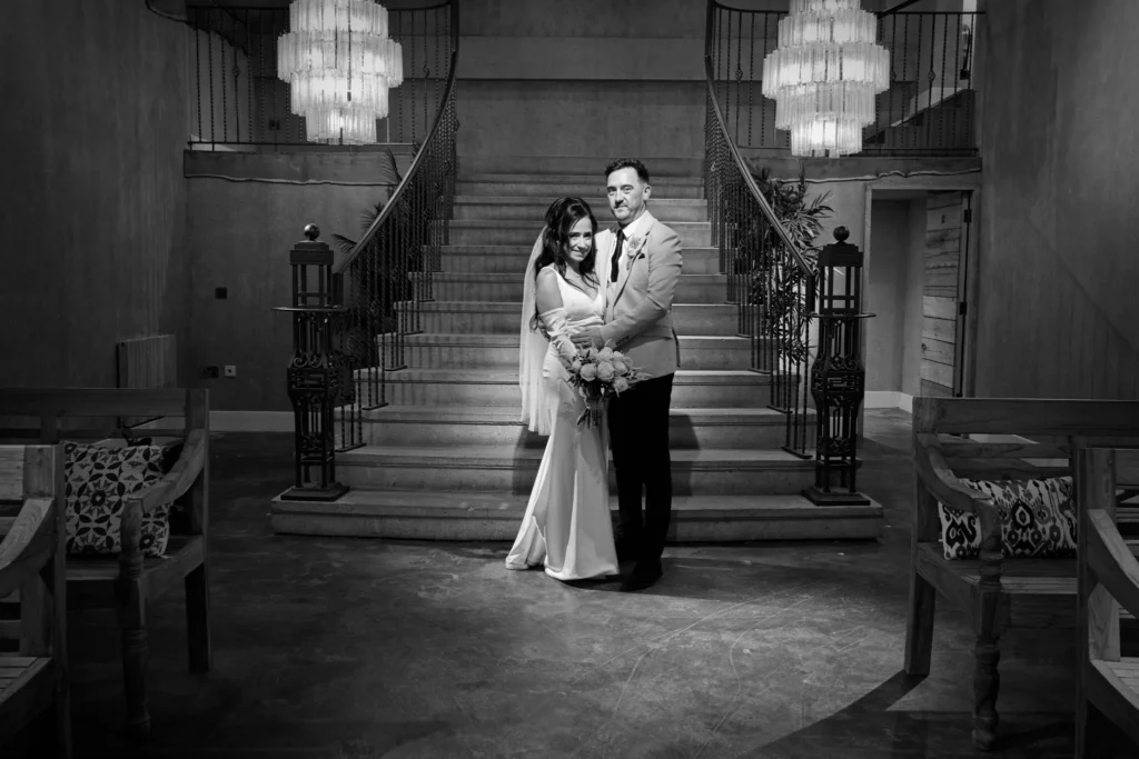 Bride and groom at the foot of a sweeping double staircase, in black and white