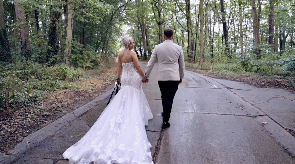 Bride and groom walk hand in hand down a woodland lane, her long train behind