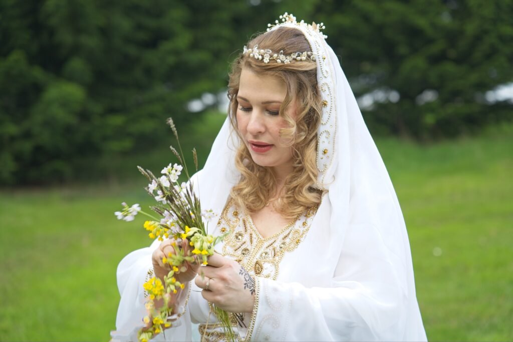 A bride with a crown of flowers and a long veil holds wild flowers