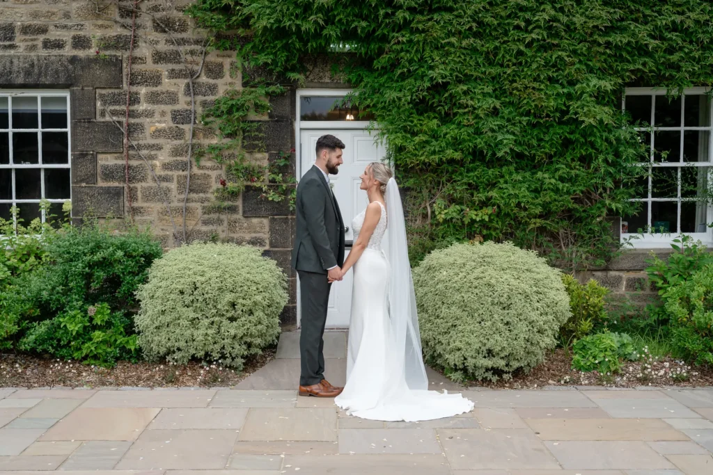 Bride and groom face each other outside an ivy-covered stone house