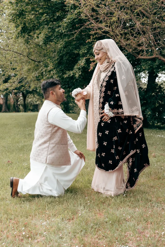 The groom kneels on the grass to take the bride’s hand at an Asian wedding
