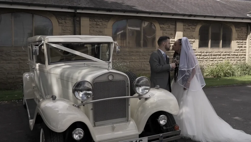 Bride and groom kiss beside a vintage wedding car