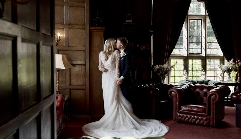 Bride and groom kiss in a wood-panelled room with leaded windows and red leather armchairs