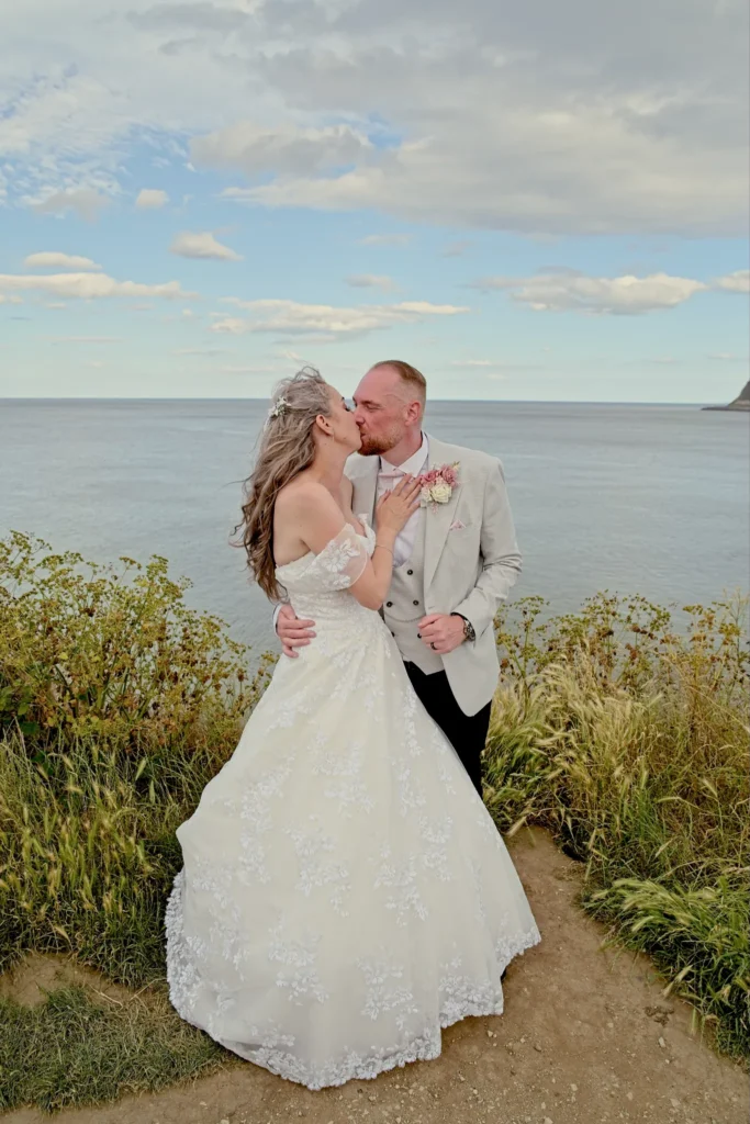 Bride and groom kiss on a clifftop path above the sea