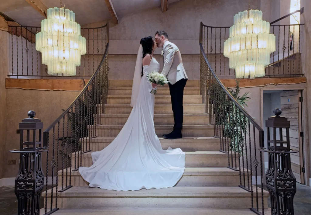 Bride and groom kissing on a grand staircase between two chandeliers