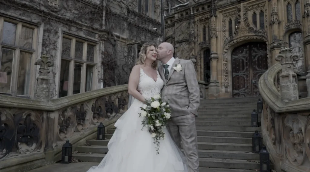Bride and groom on the carved stone steps of a Gothic hall