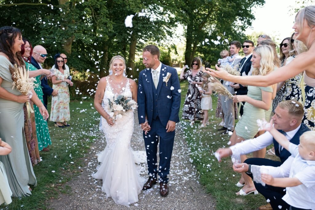 Guests throw confetti over the bride and groom on a garden path