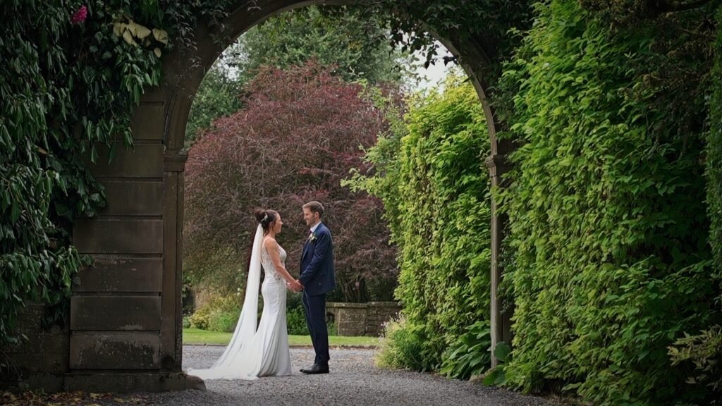 Bride and groom framed by a stone archway in the garden