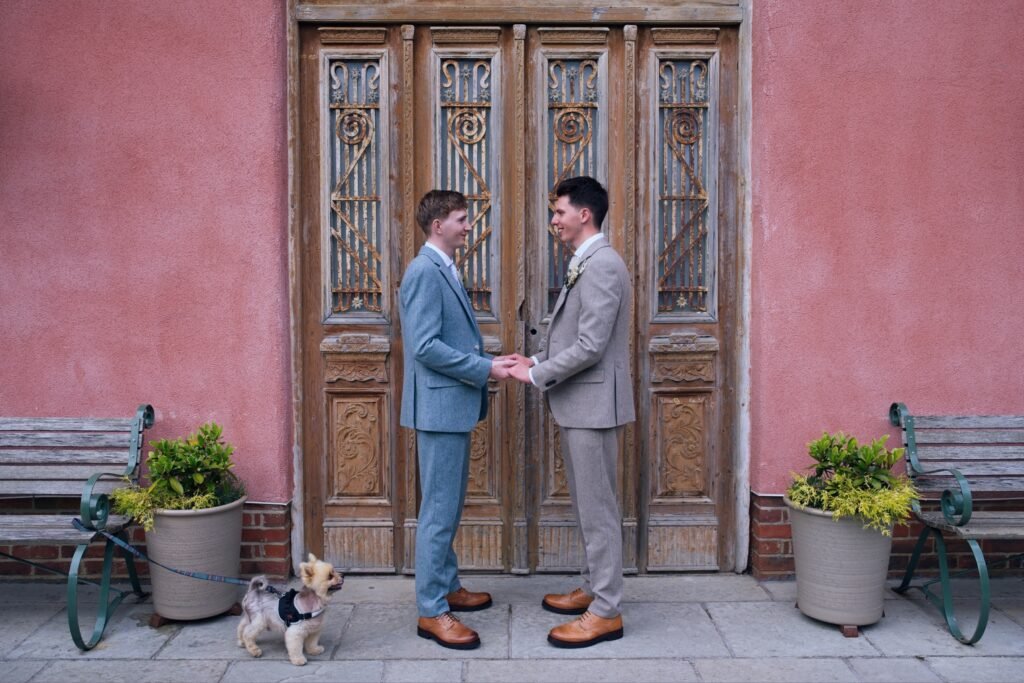 Groom and groom holding hands in front of an ornate wooden door at Le Petit Chateau