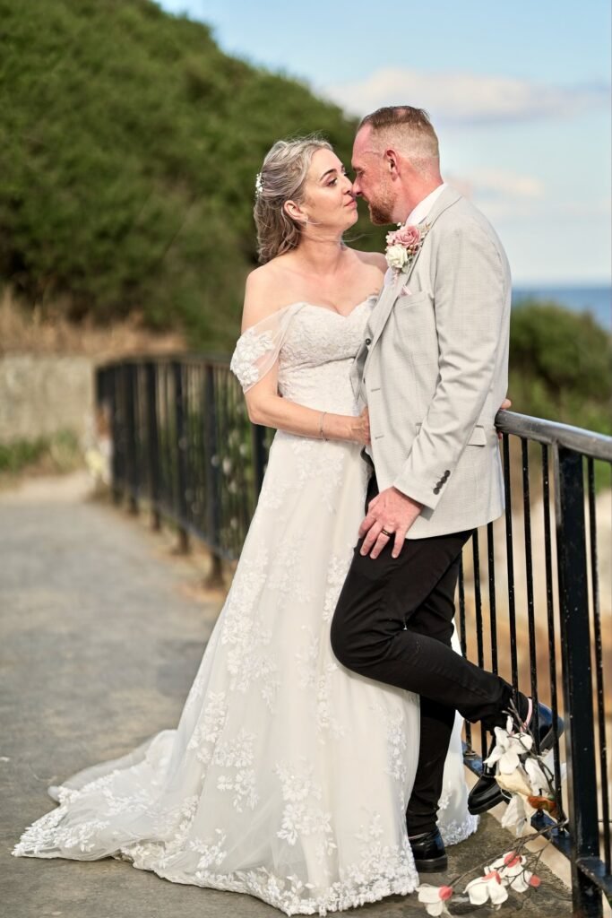 Bride and groom sharing a quiet moment by the railings of a coastal path