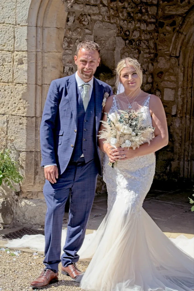 Bride and groom in front of an old stone wall and arch, in bright sunshine