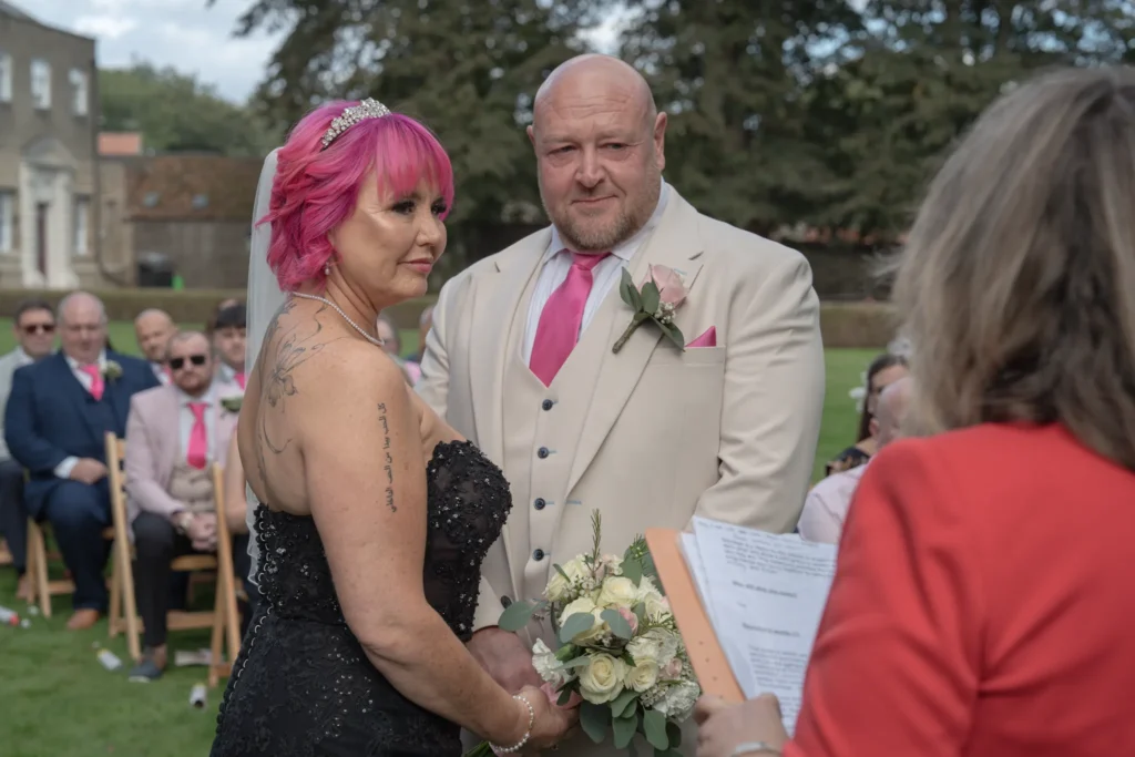 Bride and groom face the celebrant at an outdoor ceremony on a lawn