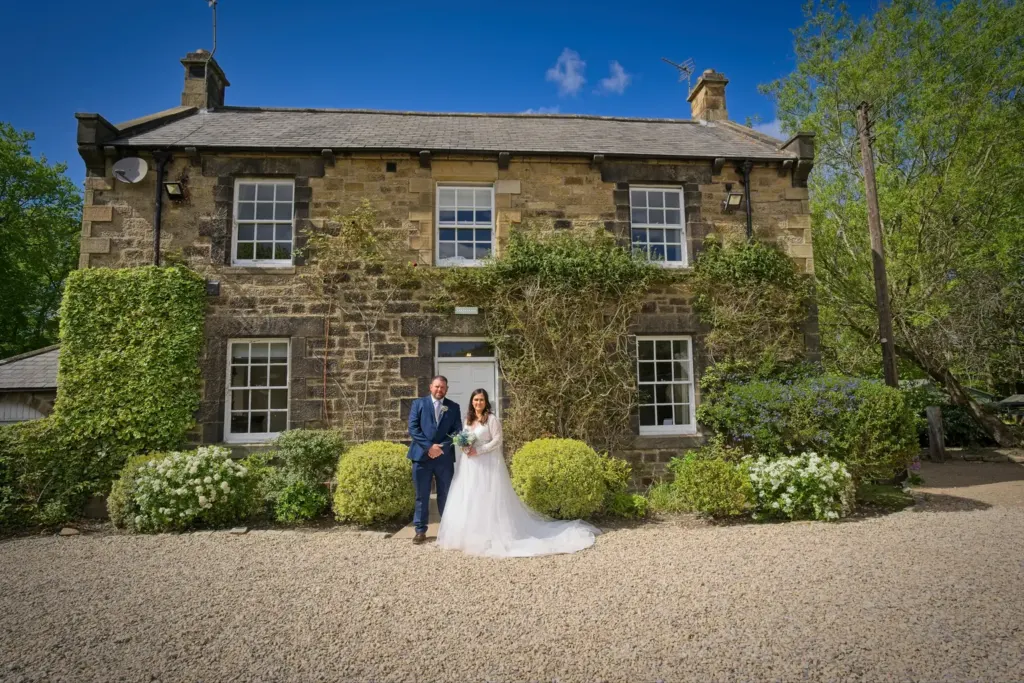 Bride and groom in front of an ivy-covered stone farmhouse under a blue sky