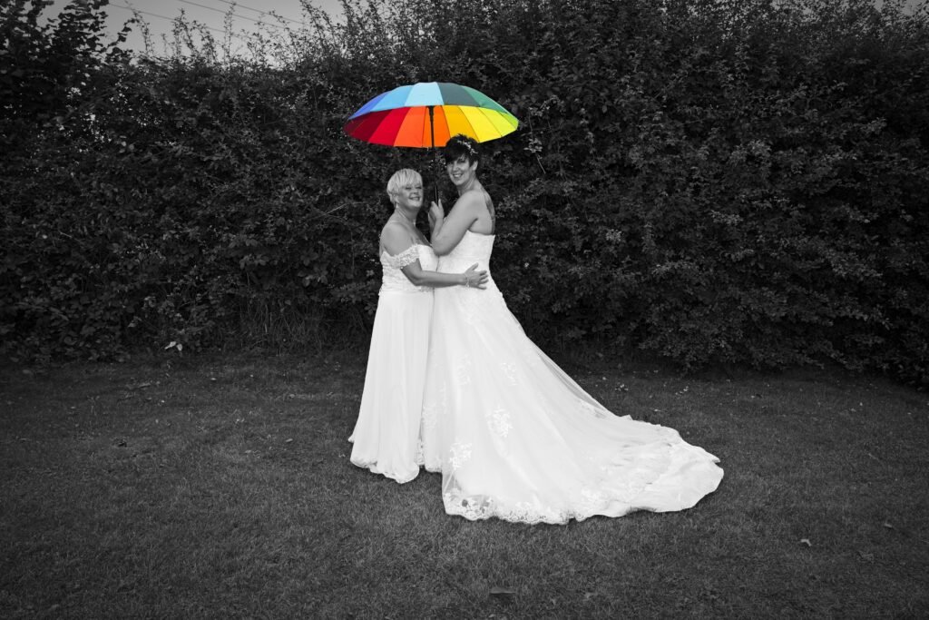 Two brides under a rainbow umbrella
