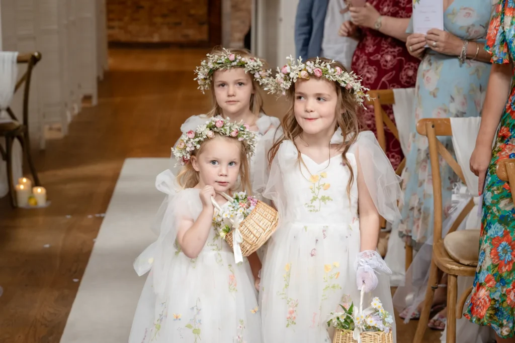 Three flower girls in flower crowns walk down the aisle with their baskets
