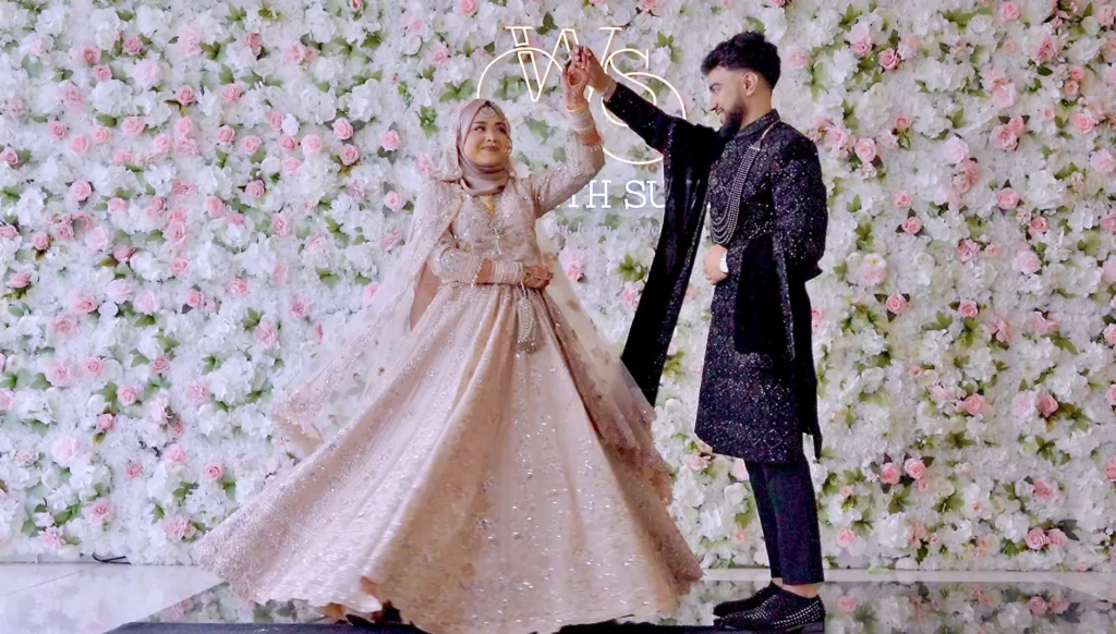 At an Asian wedding, the groom twirls the bride in front of a wall of pink and white roses