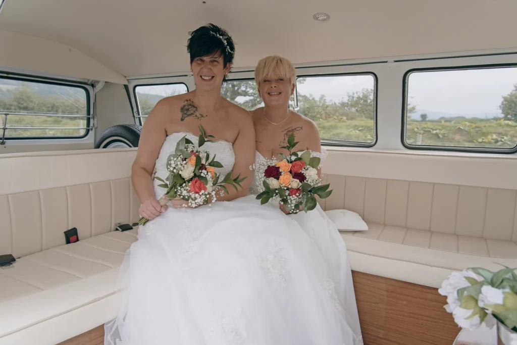 Two brides sit with their bouquets inside a cream vintage campervan