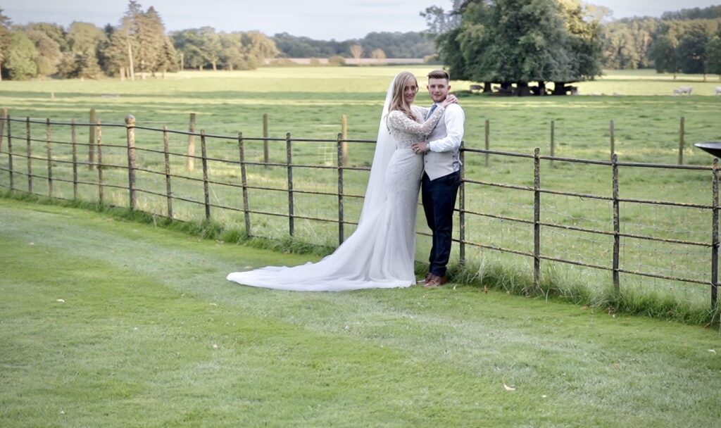 Bride and groom lean on a wooden fence in open parkland