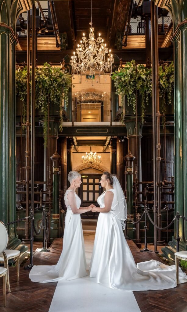 Two brides holding hands beneath a chandelier among Victorian machinery