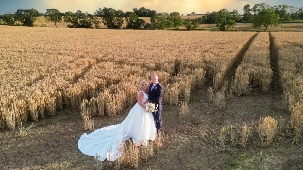 Bride and groom in a golden wheat field at sunset, seen from a drone