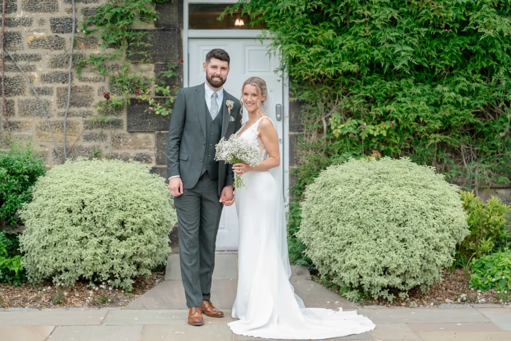 Bride and groom hand in hand at a white door between two round shrubs