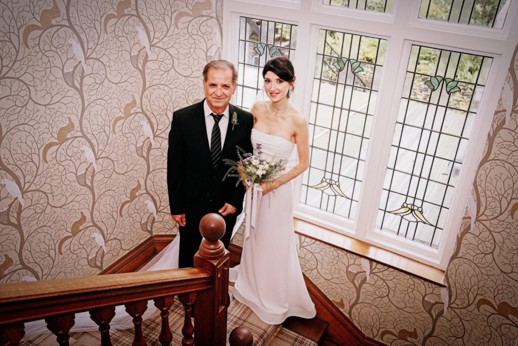 The bride and her father on the staircase by a stained-glass window