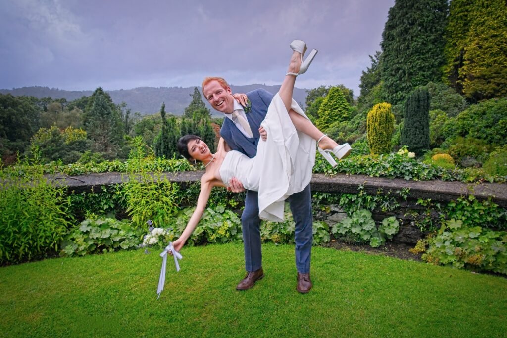 The groom lifts the bride in a garden with hills behind