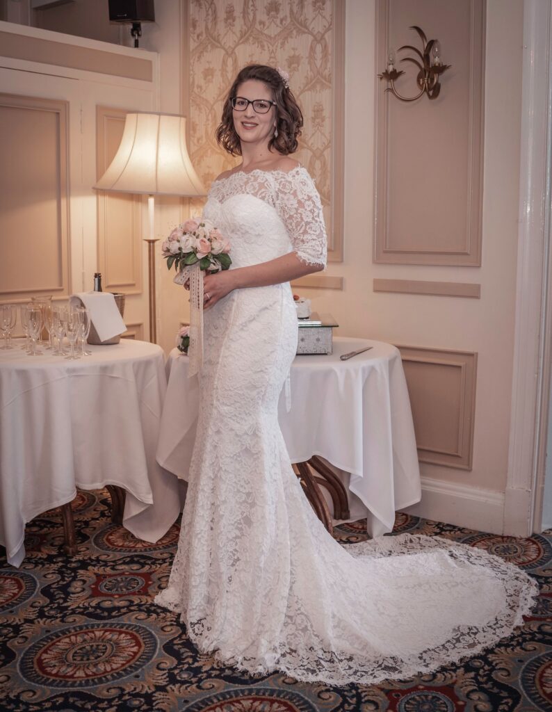 The bride in a lace gown beside a lamp in her room